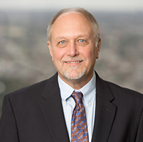 Richard Oberhelman, wearing suit, seated in front of a window overlooking New Orleans downtown